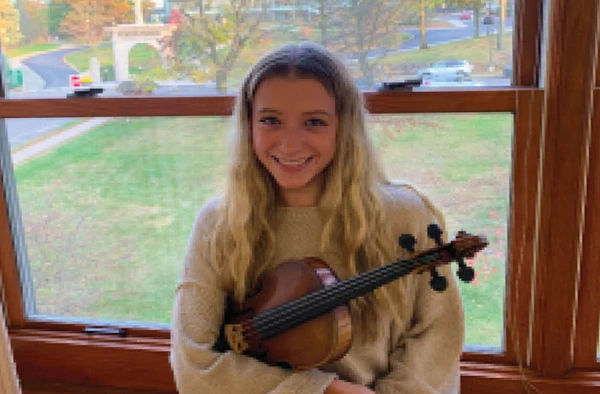 A female student leaning against a window while holding a violin.